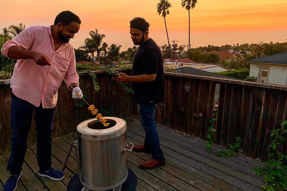 Friends cooking skewers on a GULATI home tandoor at sunset